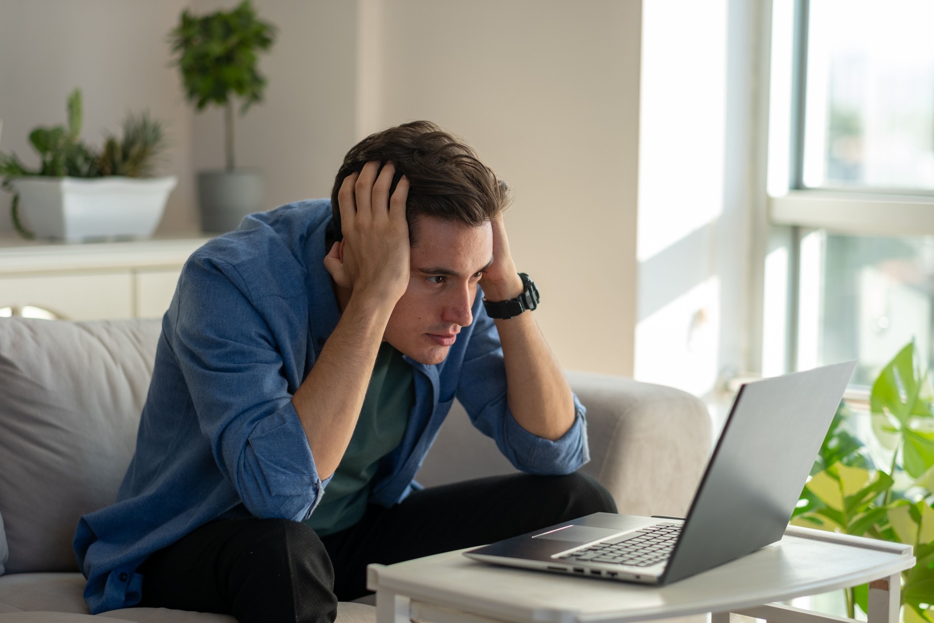 Stressed young man working from home holding head in hands